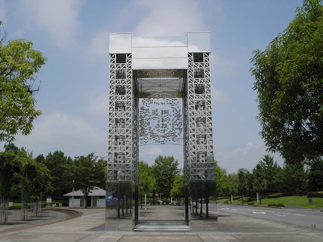 公園の敷地に銀色の脚が4本建った門が作られており、上部に銀色の玉を連ねて人の顔が浮かび上がるように作られた門の写真