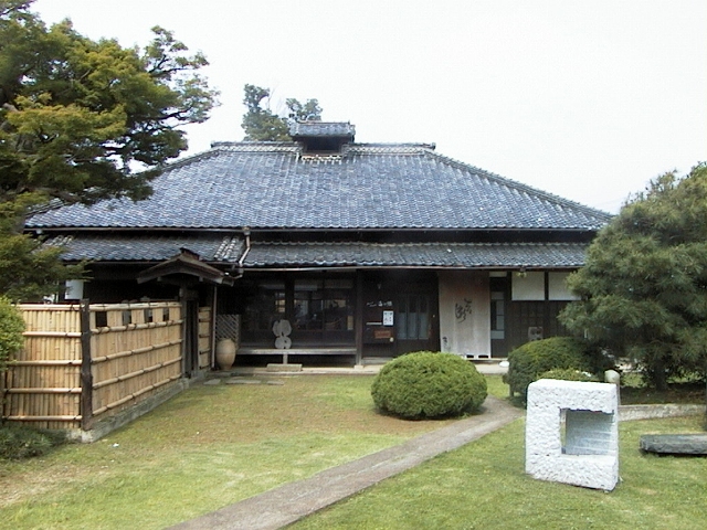 向かって左側の敷地が竹の壁で仕切られている瓦屋根の古民家の外観写真