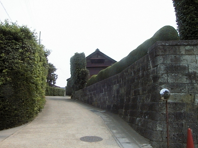 中央に坂道があり、右側に石垣、左側に生垣が続いている花室集落の写真