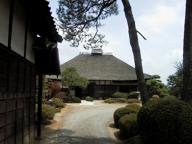 砂利道の先にきれいに手入れされた庭園と茅葺きの建物が建っている写真