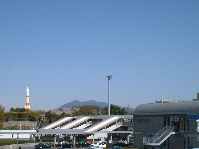 バスターミナルの外観の先にロケットと山並みが写っている写真