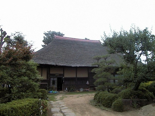 庭園の先に茅葺き屋根の民家が建っている写真