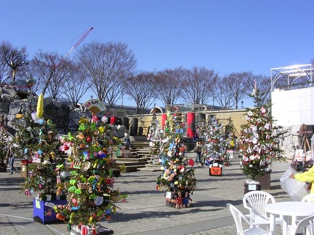 広場に等間隔にカラフルなツリーが置かれ、それぞれ個性的に飾り付けられている写真