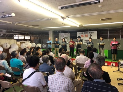 小さなステージに8名の出演者がマイクスタンドの前に立ち朗読劇を行っている様子を観客が見ている後ろ姿の写真