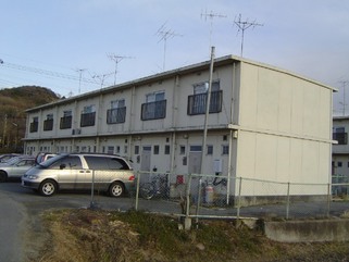 建物の前に自転車や車が駐車している2階建ての小田第二団地の玄関側を右斜めから撮影した写真