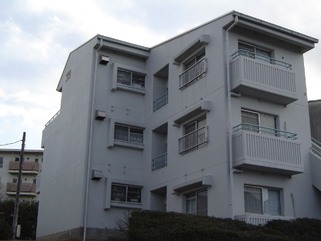 生垣に囲まれた3階建ての吾妻住宅を下からアップで撮影した建物外観の写真