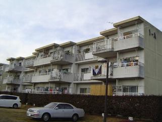 生垣の手前に駐車場が設けられている3階建ての金田住宅をバルコニー側から撮影した写真