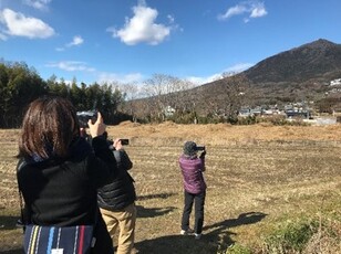 奥に見える山に向かってスマートフォンをかざし、地質体験アプリを利用する様子の写真