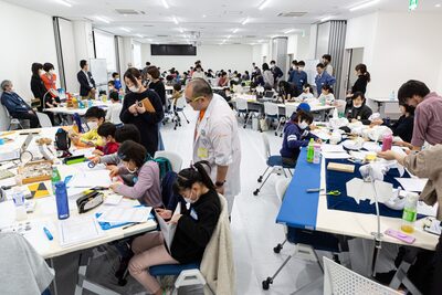 子供たちがグループごとに分かれて作業をしている横で講師が見守っている体験型科学教育イベントの写真