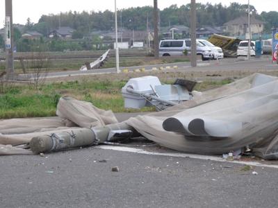 根元から折れた電柱や信号機と、大きな看板が車の上に乗っている写真