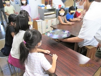 何かを回している所をこども達にみせている実験隊の様子の写真