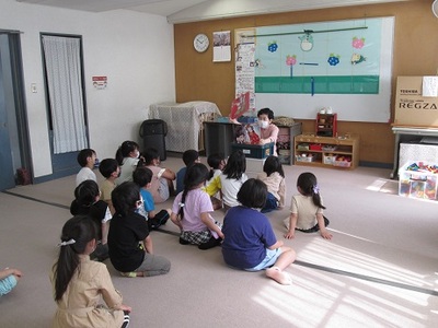 子ども達の前で女性が紙芝居を読んでいる写真