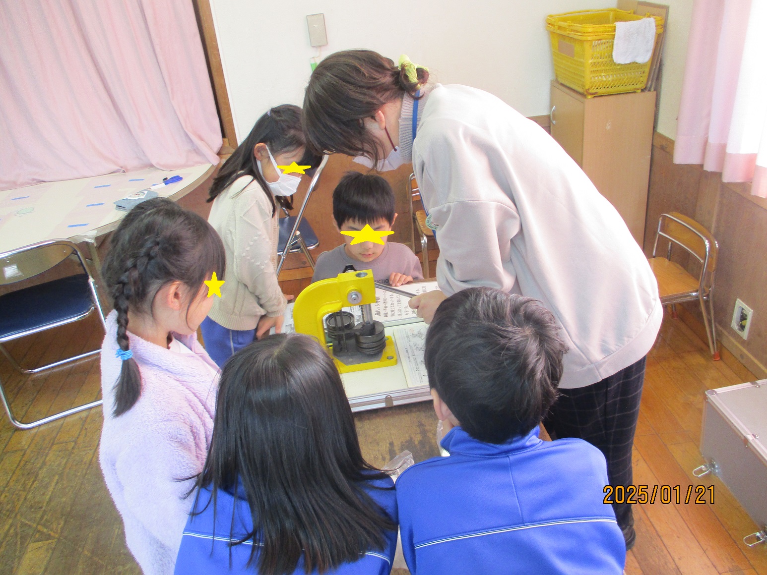 缶バッチマシーンを操作する先生と見守る子供たち
