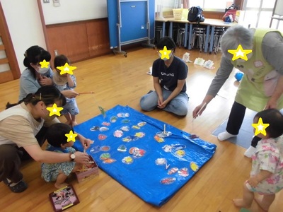 小さなビニールシートの上に置いたイラストの魚を釣ろうとしている親子の写真