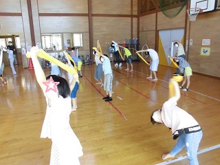 体育館で子どもたちがタオルをつかってストレッチをしている写真