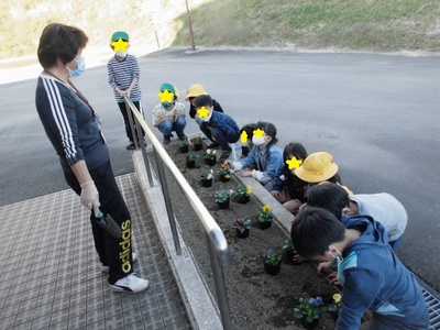 黄色や青色のカラフルな花が花壇に置いてあるのを見ている子供たちの写真