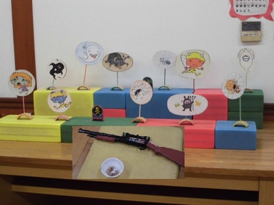 鬼やばい菌、蜂などのイラストが描かれた的が並び、射的の銃が玉と一緒に置かれている写真