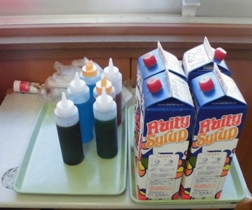 かき氷にかけるためのシロップと練乳が入っている容器が並んでいる写真
