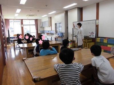 ホワイトボードを使い説明する先生と、席に座り話を聞く子供たちの写真