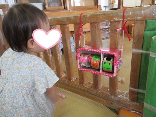 うさぎやカエル、おにぎりなどの絵が付いた回る手作りおもちゃに興味を示す0歳児