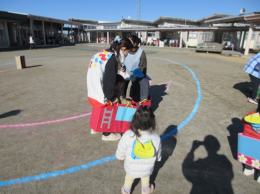 所庭に段ボールで作った消防車や自動車に入りコースを入らせる1.2歳児
