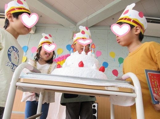 大きな誕生日ケーキのロウソクを吹き消すまねをする誕生者