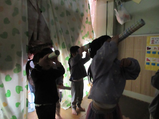 暗い部屋(夜の森)で望遠鏡に見立てた筒で蝙蝠を探す子どもたち