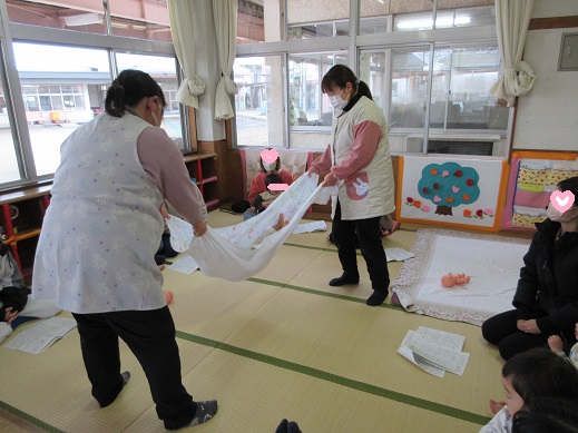 タオルケットに横になり、『ことりことり』の歌に合わせ、保育士に揺らして貰っています。