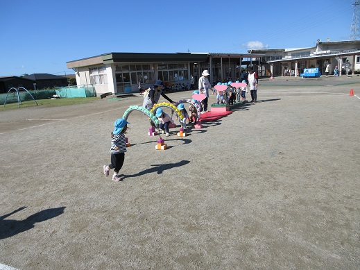 巧技台の蓋を並べた橋を渡りお花のトンネルをくぐる2歳児