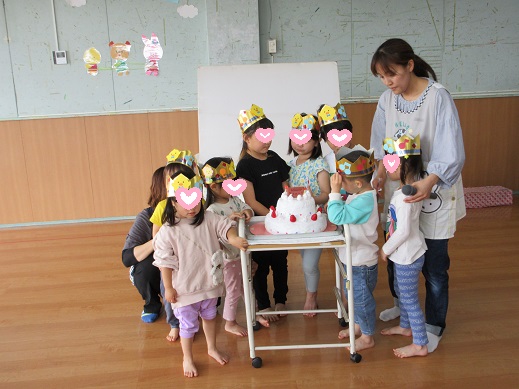 4月生まれの子どもたちが大きなケーキのロウソクを消そうとしているところ
