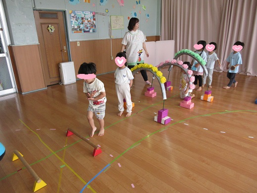 花のトンネルをくぐり小さなハードルを跳ぶ3歳児