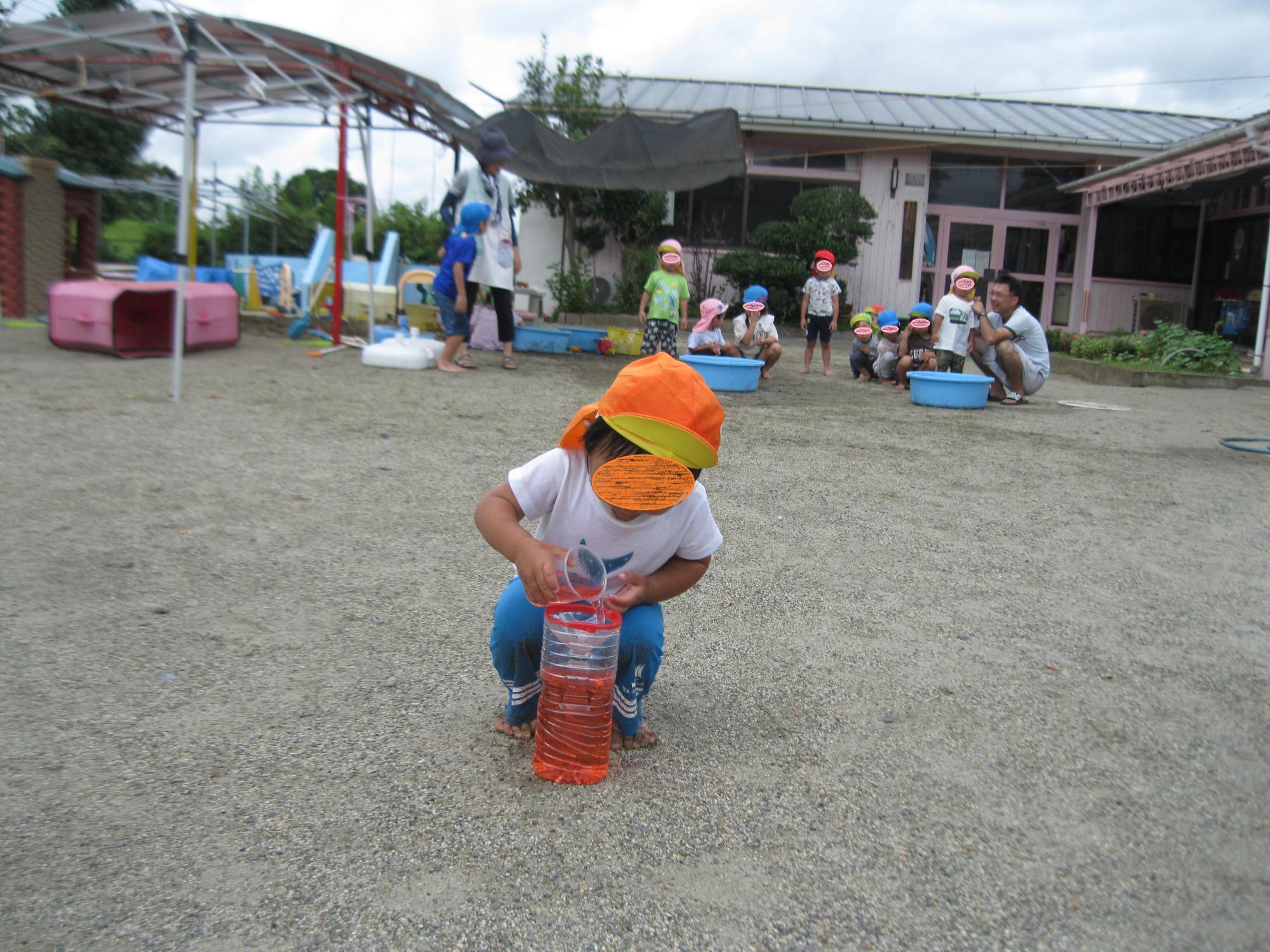 1歳の男の子がペットボトルへ赤色の水を上手に入れています。