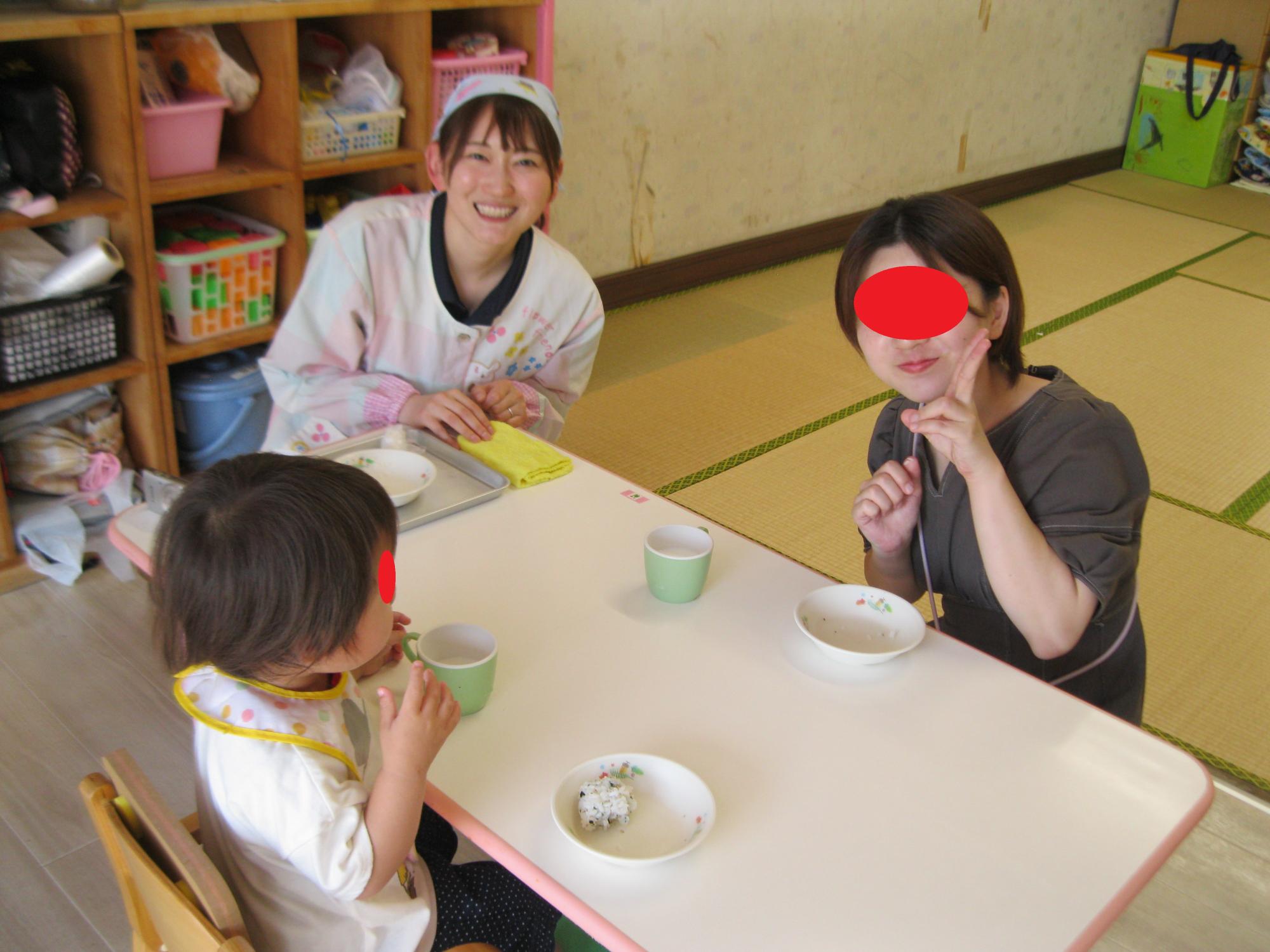 1歳児が先生とお母さんと一緒におやつのわかめご飯を食べています。
