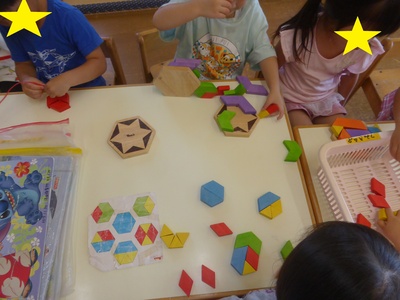 ひし形や三角形などのパズルを組み立てて遊んでいる子供たちの写真