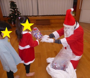 サンタクロースの衣装を着た先生から子供たちが一人ずつ並んでプレゼントを貰っている様子の写真