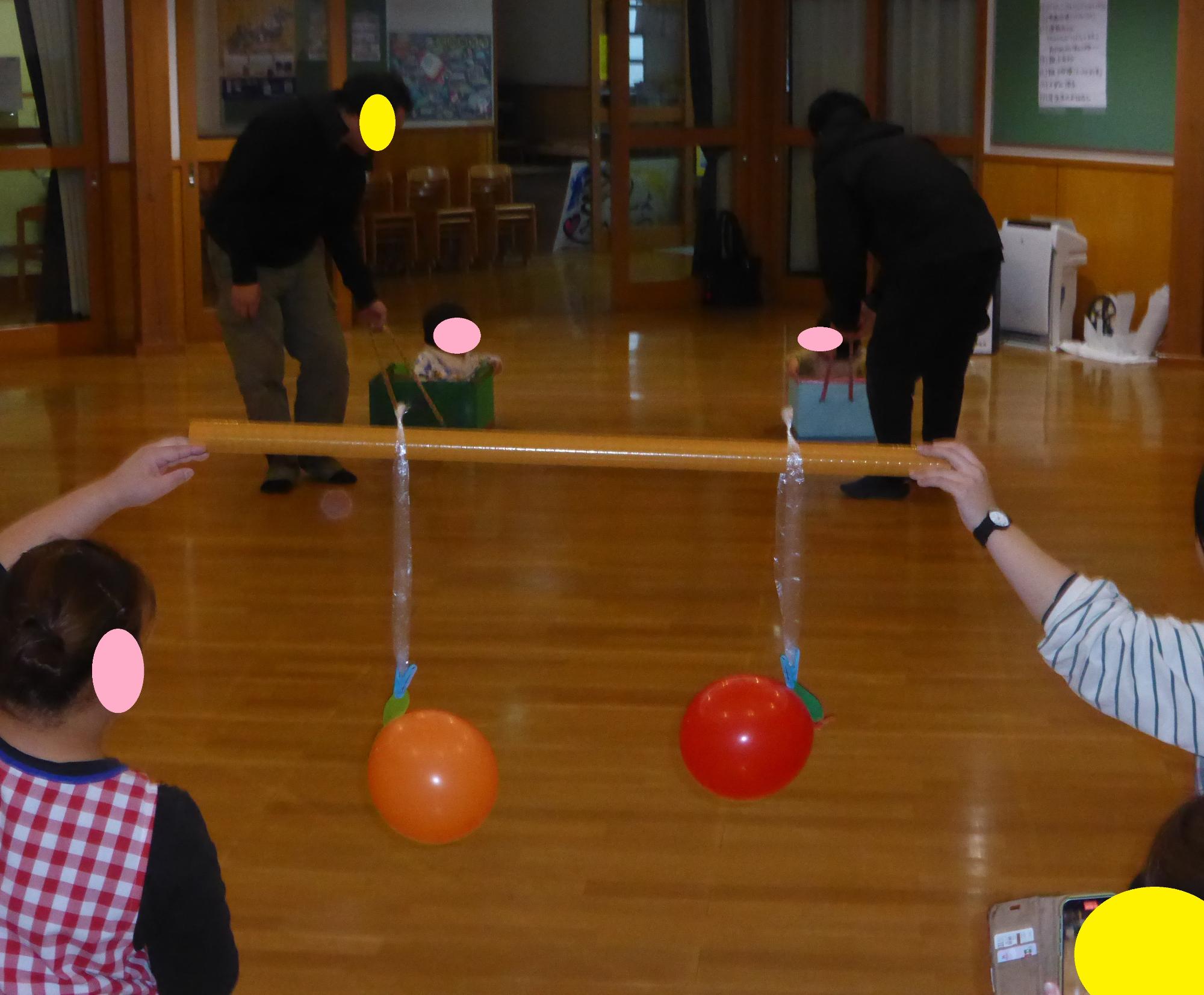 小さな子が段ボールの車に乗って、おうちの人に引いてもらっています。