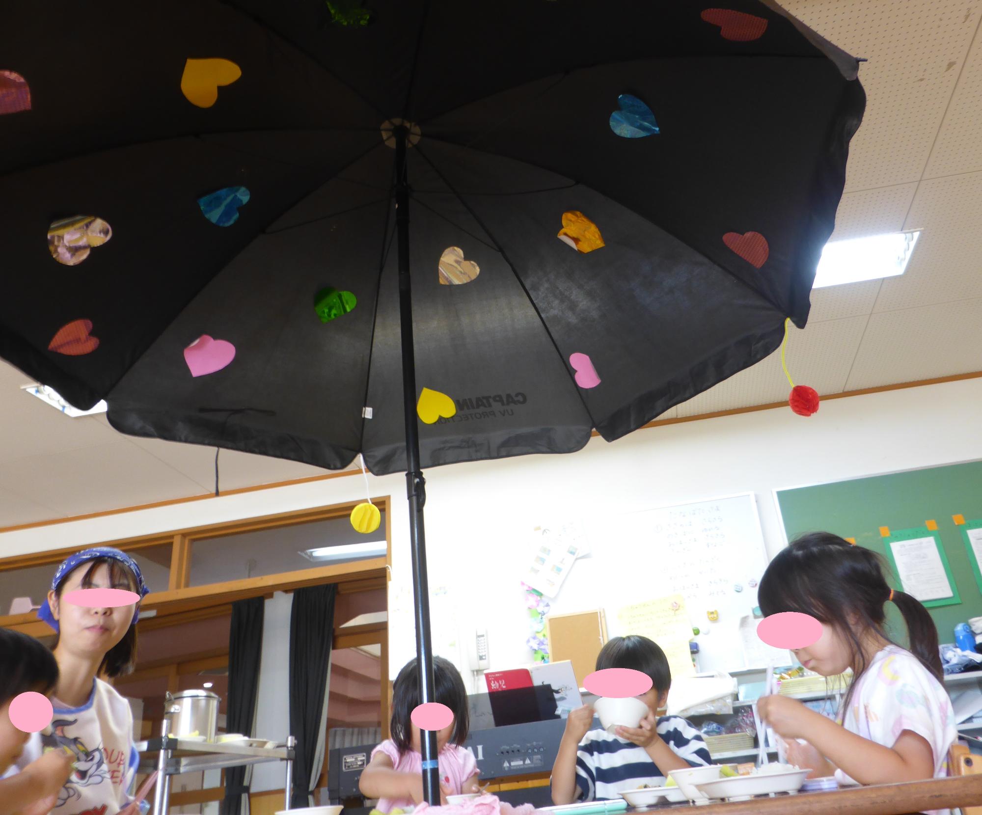 パラソルの下で、会話しながら給食を食べています。