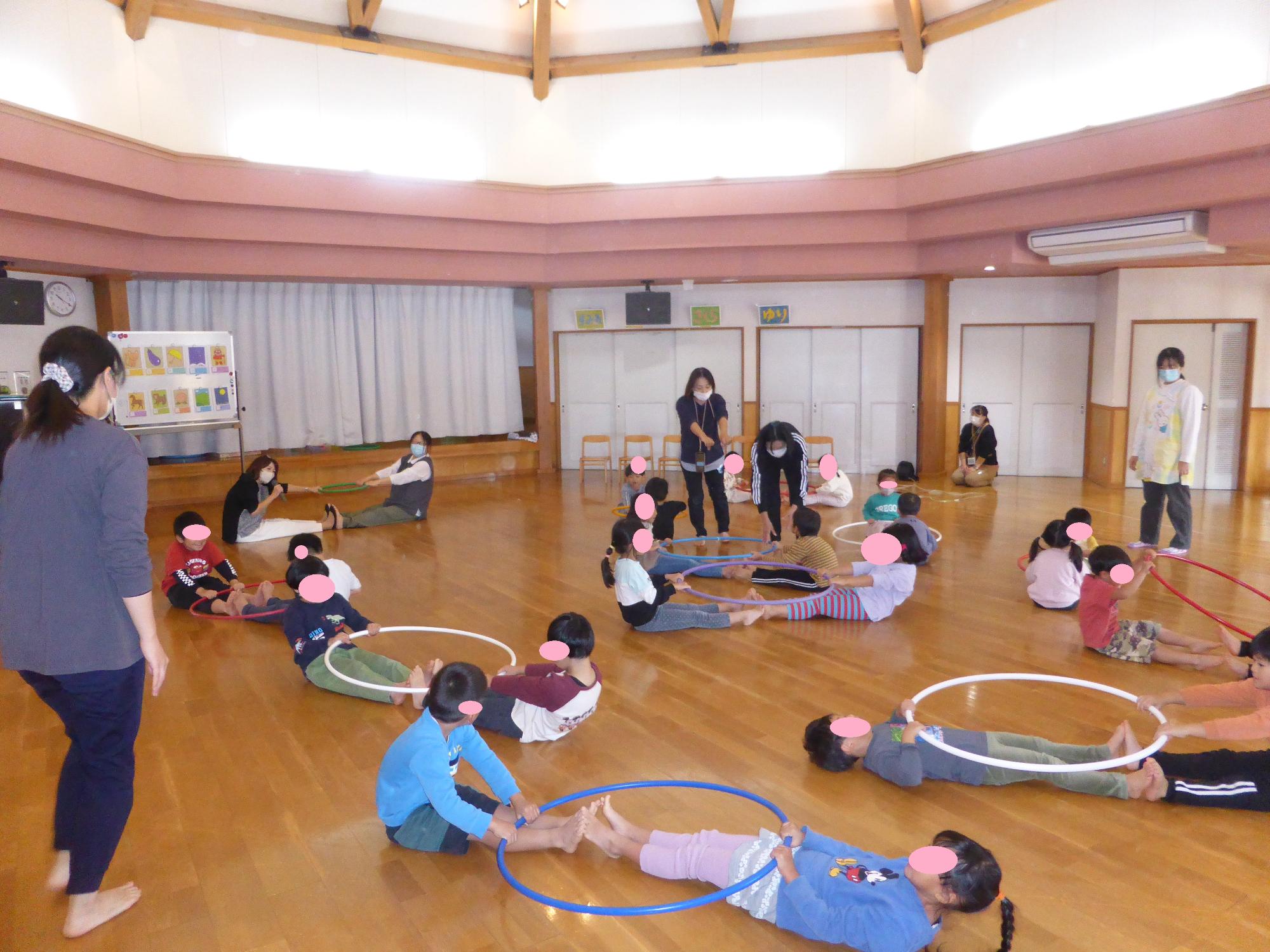 子どもたちが、講師の先生にリトミックを教わり、フラフープで遊んでいます。