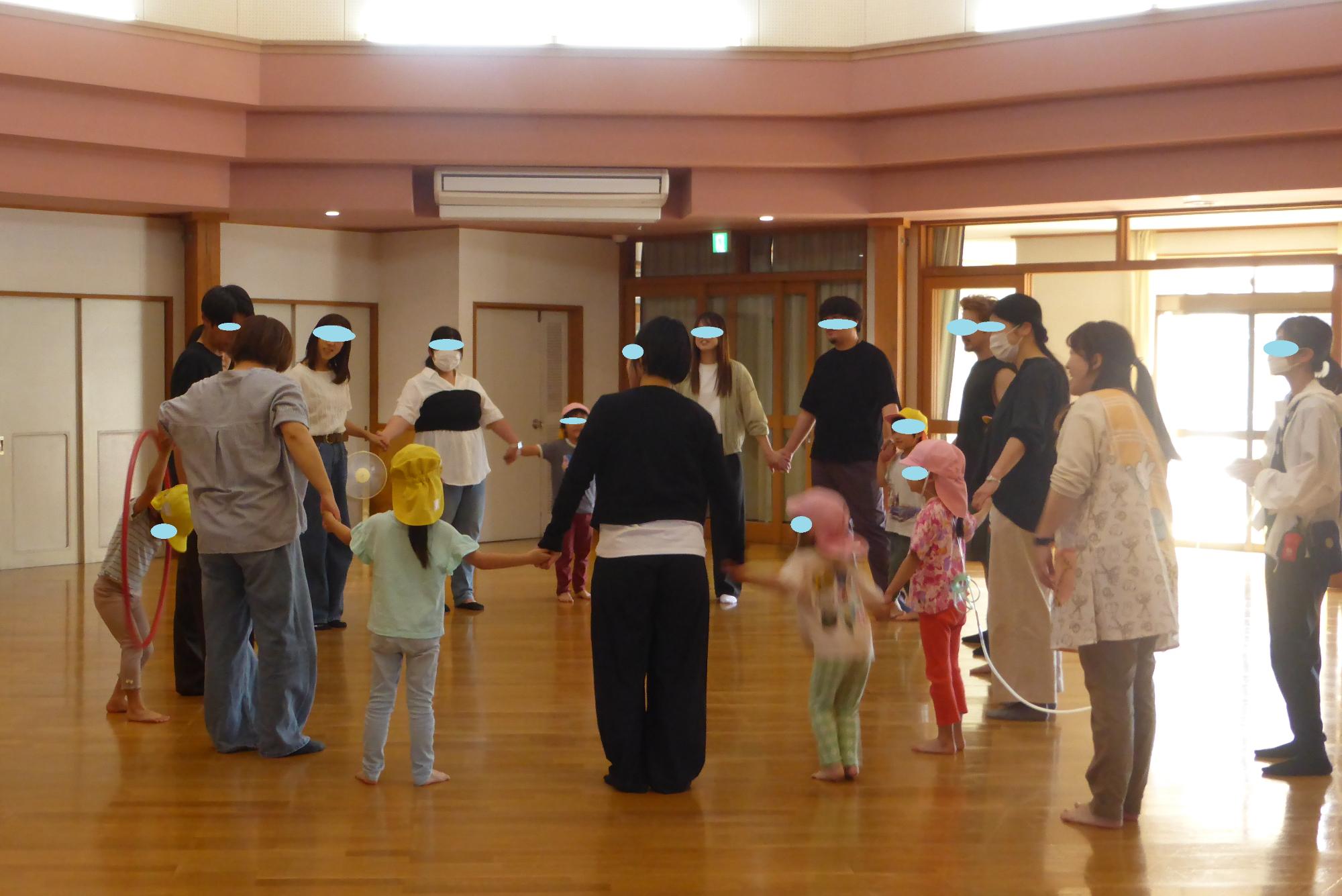 すみれ組の子どもたちが、保護者と手をつなぎ大きな輪になって、フラフープ渡しを楽しんでいます。