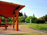 右側の芝生広場の中央にベンチが設けられ、左手前に2つのテーブルが設置された大きな東屋の写真
