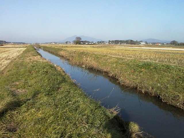 奥に山脈、周囲には田園が広がり、中央を緩やかに流れる谷田川の写真