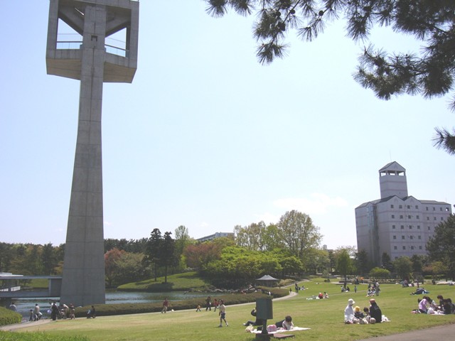 展望塔が建っている公園の芝生にシートを敷いて座っている家族や遊んでいる親子で賑わっている様子の写真