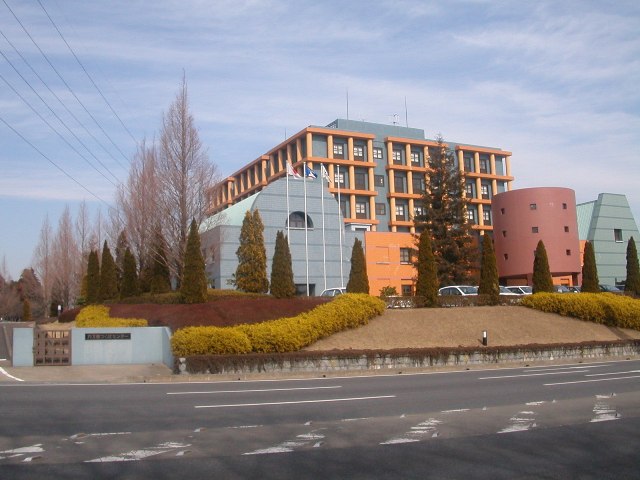 様々な色に塗られた壁の建物がカスミつくばセンターの敷地内に複数建てられており、一番奥に建っている建物はオレンジ色の柱で覆われている外観の写真