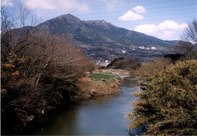 中央に桜川が緩やかに流れ、両岸に河畔林が生い茂り間から筑波山が覗いて見える写真