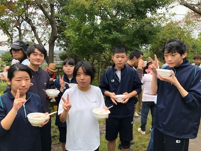 芝桜植栽イベントに参加した中学生たちが豚汁が入っている容器を片手にカメラに向かってピースサインをしている写真