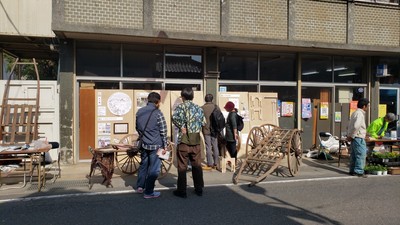 建物の手前の歩道上に展示されている大八車を見ている人達の写真