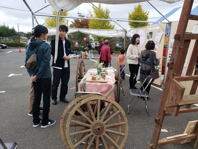 展示ボードの前や大八車の前で見学者に展示物の説明を行っている谷田部市街地のオータムフェアでの出展の様子の写真