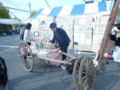 展示ボードの前に置かれた大八車の前にミニチュアの大八車を展示している男性の写真