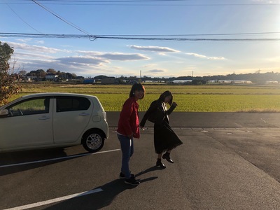晴天の下、1台の白い車の前でポーズをとっている2名の女性の写真