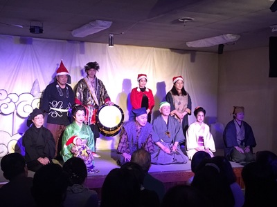 クリスマス伊賀七の演劇に10名の出演者がステージに集まり中央に座っている男性が観客席に向かって話をしている写真